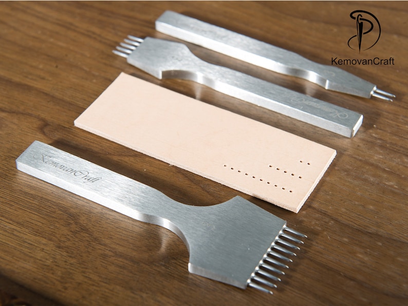 May include: A collection of silver leatherworking tools, including punches and a strip of beige leather with punched holes. The tools are arranged on a wooden surface, showcasing their design and functionality for crafting.