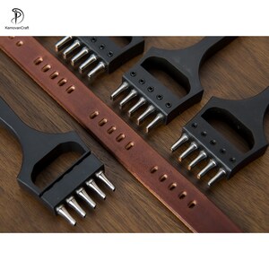 May include: Leatherworking tools, including a brown leather strap with evenly spaced holes and several black metal punches with silver prongs. The tools are arranged on a wooden surface, showcasing the craftsmanship.