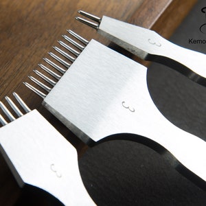 May include: Three silver leathercraft tools with multiple prongs, each marked with the number "3". The tools are arranged on a wooden surface, with the "KemovanCraft" logo visible in the background. These tools are used for leatherworking.