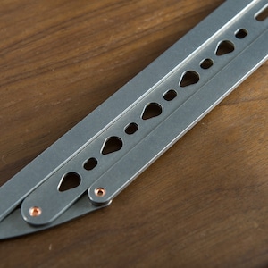 May include: A silver folding knife with a row of holes along the blade. The knife has a copper-colored pin at the joint.