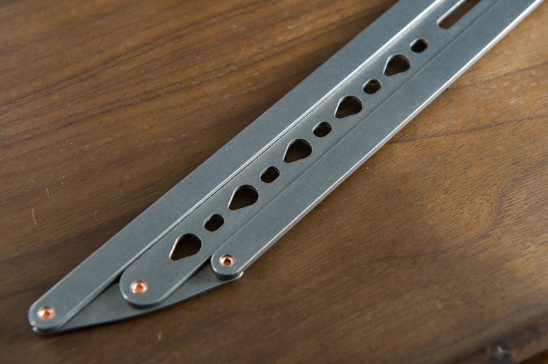 May include: A silver folding knife with a row of holes along the blade. The knife has a copper-colored pin at the joint.