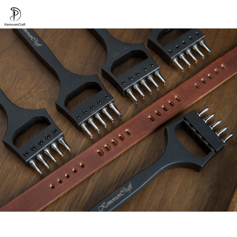 May include: A collection of black leatherworking tools with silver prongs, arranged near a brown leather belt. The tools are stamped with the text "KemovanCraft". The tools are used for creating holes in leather.