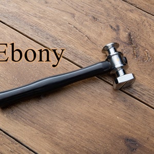 May include: A silver hammer with a black wooden handle, labeled "Ebony", on a wooden surface.