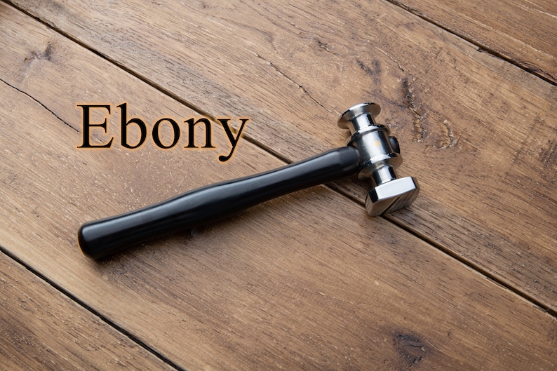 May include: A silver hammer with a black wooden handle, labeled "Ebony", on a wooden surface.