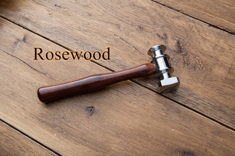 May include: A rosewood handled hammer with a silver head. The hammer has a square head with a beveled edge. The word "Rosewood" is written in orange letters on a wooden surface.