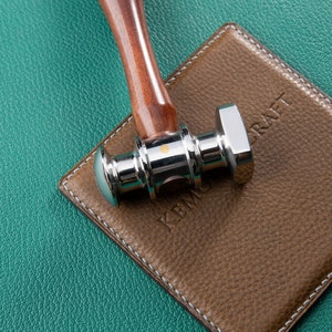 May include: A silver and wooden hammer with a textured brown leather surface with the word "KRAFT" embossed on it.