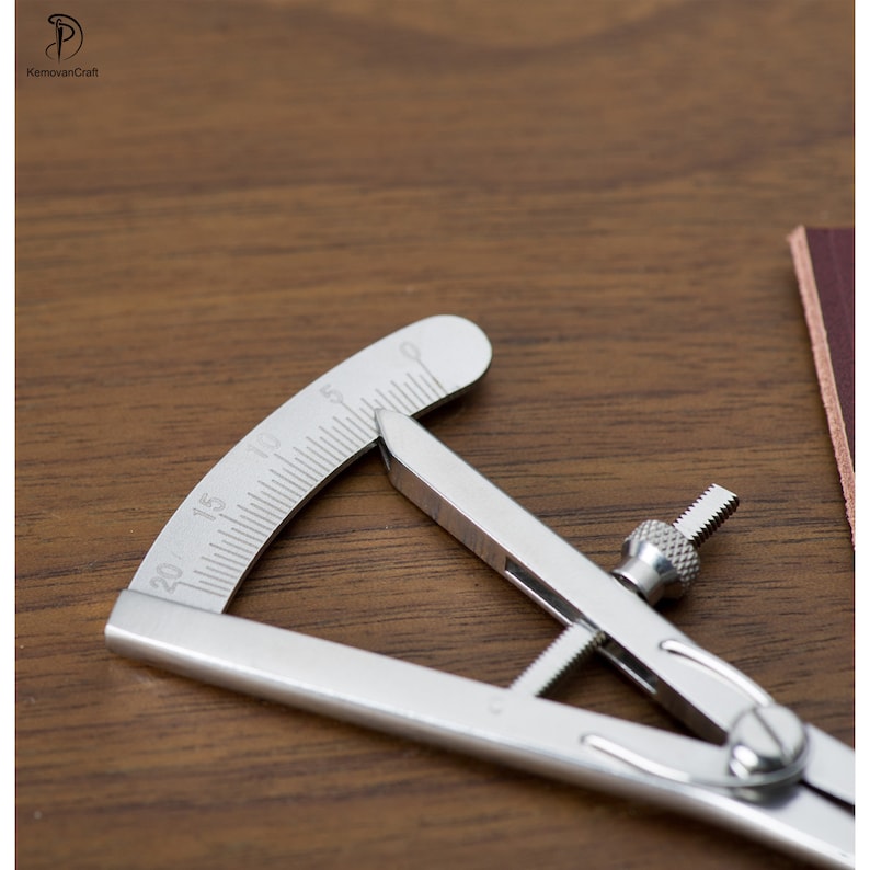 May include: A silver metal leather measuring tool with a protractor and a screw adjustment. The tool is on a wooden surface.