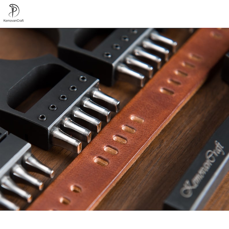 May include: Close-up of leather crafting tools and a brown leather strap. The tools are black with silver metal punches. The leather strap has evenly spaced holes. The tools are for leather working.