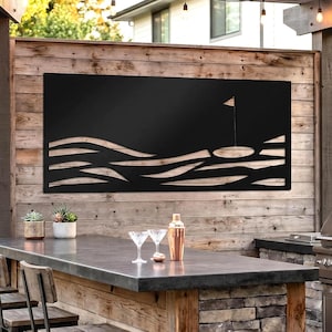 May include: Black metal golf course wall art with a flag and undulating lines, mounted on a wooden wall. The outdoor setting includes a bar with stools, a grill, and string lights.