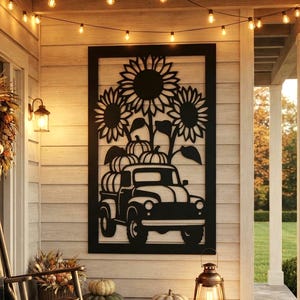 May include: A black metal wall art piece featuring a vintage truck carrying pumpkins under sunflowers, displayed on a porch with a rocking chair, a wreath, string lights, a lantern, and various pumpkins arranged on the floor.