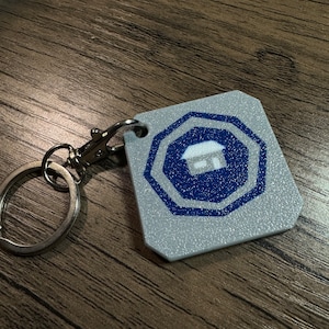 May include: A silver key chain with a gray and blue octagonal tag featuring a white house icon. The tag has a textured surface.
