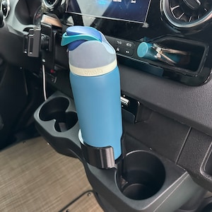 May include: A blue and teal water bottle with the word "owala" printed on it is in a black cup holder in a car. The cup holder is attached to the side of the driver's seat.
