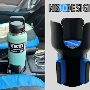 May include: A black 3D printed car cup holder with blue magnetic bases. The cup holder is designed to hold a Yeti Rambler 46 oz bottle. The bottle is light blue and has a black lid and handle. The text "YETI RAMBLER 46 oz BOTTLE" is printed on the bottle.