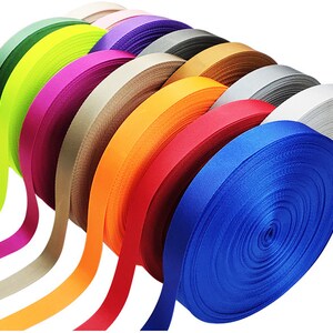 May include: A collection of colorful ribbon spools in various shades of green, yellow, pink, beige, orange, red, blue, and gray. The ribbon is wound tightly on the spools.