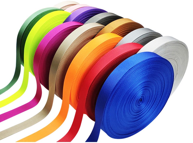 May include: A collection of colorful ribbon spools in various shades of green, yellow, pink, beige, orange, red, blue, and gray. The ribbon is wound tightly on the spools.