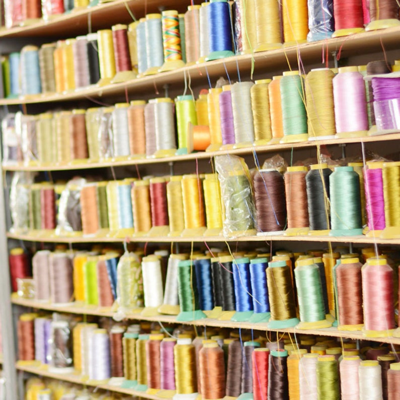 Pode incluir: Uma prateleira cheia de carret&eacute;is de fio colorido. O fio est&aacute; organizado por cores e est&aacute; cuidadosamente arrumado nas prateleiras.
