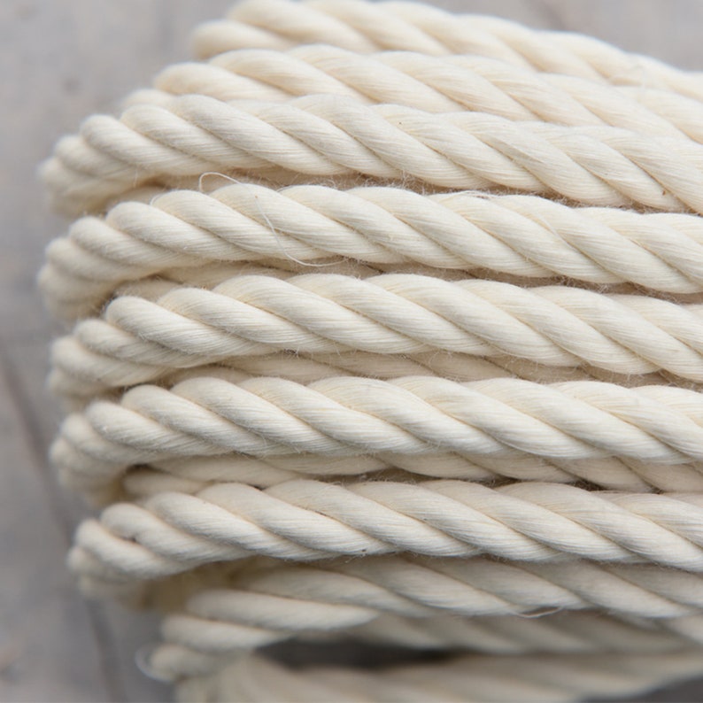 May include: Close-up of a thick, white cotton rope. The rope is tightly wound and has a soft, natural texture.
