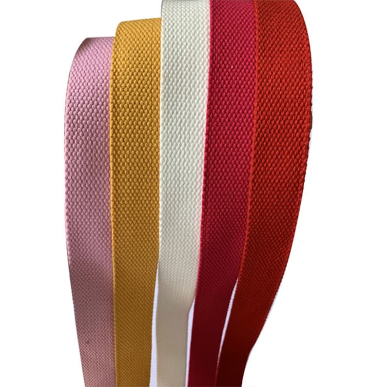May include: Five different colors of cotton webbing, including pink, yellow, white, red, and orange. The webbing is flat and woven.