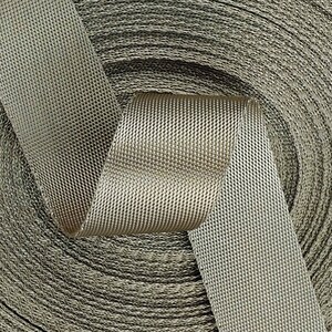 May include: A close-up of a roll of beige webbing with a textured surface. The webbing is woven with a diamond pattern.