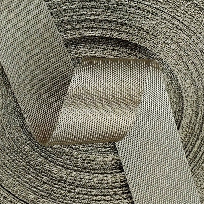 May include: A close-up of a roll of beige webbing with a textured surface. The webbing is woven with a diamond pattern.
