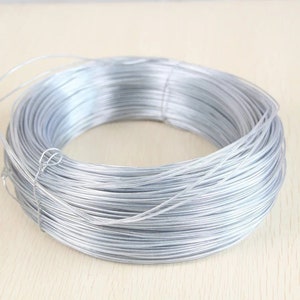 Puede incluir: Una bobina de alambre galvanizado de color plateado. El alambre está enrollado apretado y parece estar hecho de metal.