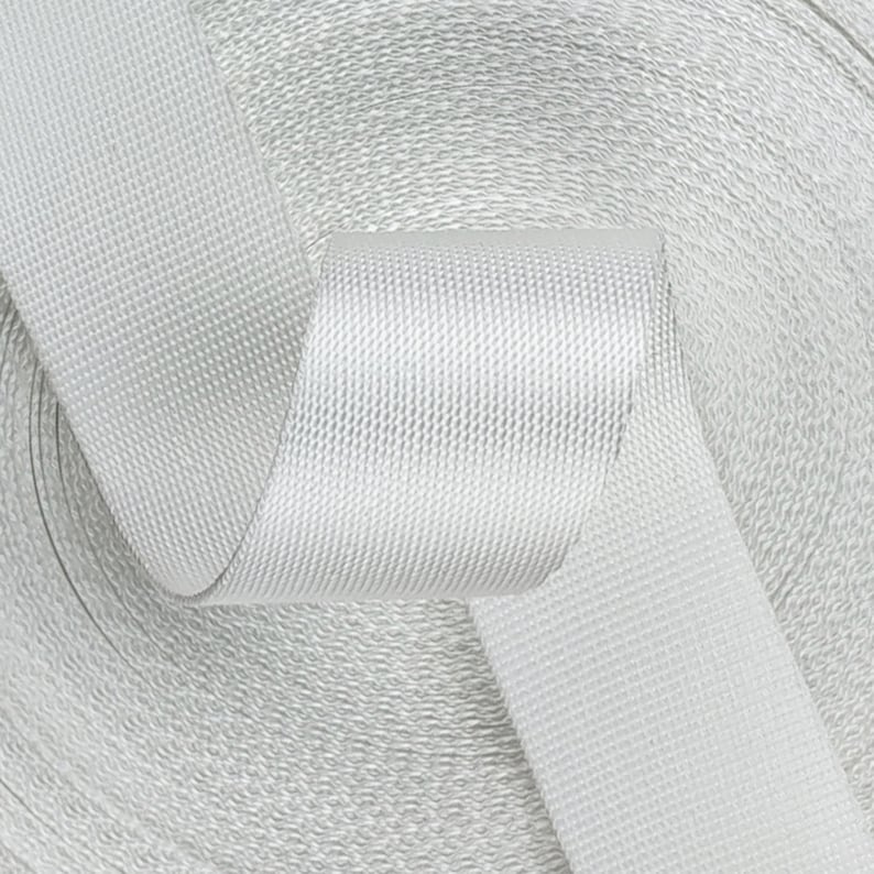 May include: A roll of white nylon webbing, a type of strong, durable fabric often used for straps, belts, and other applications.