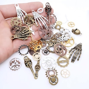 Könnte beinhalten: Sortiment an silbernen und bronzenen Steampunk-Anhängern, darunter Zahnräder, Schädel und Skeletthände. Die Anhänger sind auf einer Hand verstreut.