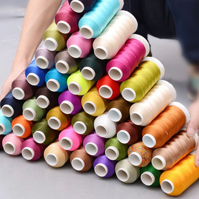 Pode incluir: Uma cole&ccedil;&atilde;o de carret&eacute;is de fio coloridos dispostos em forma de pir&acirc;mide. Os carret&eacute;is s&atilde;o feitos de v&aacute;rios materiais, incluindo algod&atilde;o, poli&eacute;ster e seda. As cores do fio incluem vermelho, laranja, amarelo, verde, azul, roxo, rosa e branco.