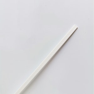 May include: A white, thin, rectangular strip of material. It has a textured surface and is slightly angled.