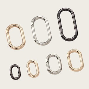 May include: A collection of seven oval-shaped spring gate rings in various metallic finishes, including gold, silver, and gunmetal. Each ring features a hinged opening mechanism, allowing for easy attachment to bags, keychains, or jewelry items.