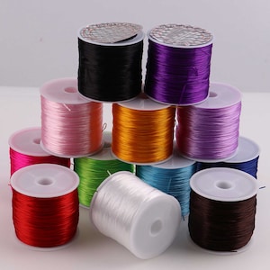 May include: Assortment of colorful elastic string spools in various colors, including black, purple, pink, orange, light purple, green, white, blue, red, and brown.