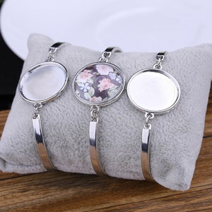 May include: Three silver bangle bracelets with round glass charms. The center charm has a floral pattern in pink, white, and green. The other two charms are clear.
