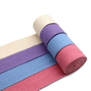 May include: Four rolls of cotton webbing in different colours: beige, purple, blue, and pink. The webbing is woven with a textured pattern.