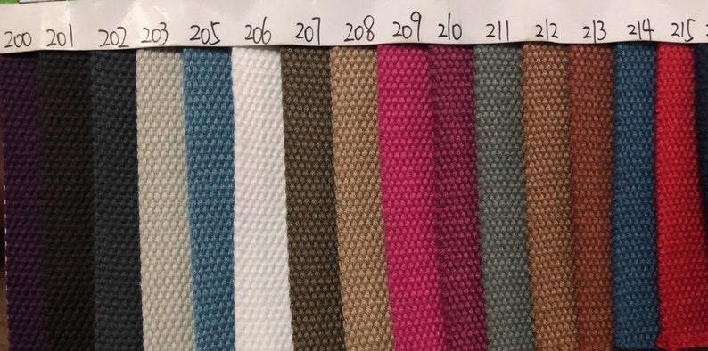 May include: A swatch card with 16 different fabric samples. The samples are arranged in a row from left to right. The colors of the samples are: purple, black, dark gray, light gray, blue, white, brown, beige, pink, dark gray, brown, orange, dark blue, red, and dark blue.