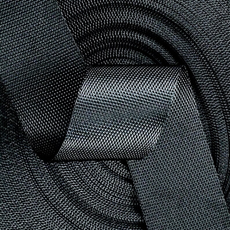 May include: A close-up of a black woven fabric with a textured pattern. The fabric is folded and twisted, creating a knot-like shape.