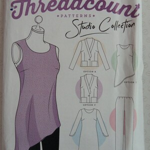May include: A sewing pattern package with the text "Threadcount PATTERNS Studio Collection". The package features illustrations of clothing options, including a vest, dress, and pants. The main image shows a purple asymmetrical top on a mannequin.