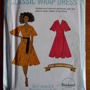 May include: A sewing pattern package for a classic wrap dress. The package features illustrations of the dress in orange and red, with the text "CLASSIC WRAP DRESS" at the top. Includes Girls' sizes 3-8 and Women's sizes S-XL.