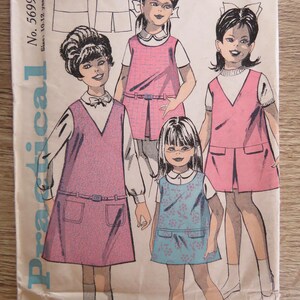 Pode incluir: Um envelope de molde de costura vintage com a etiqueta Practical No. 5699, tamanho 10-12 anos. A ilustração apresenta quatro figuras vestindo vestidos sem mangas sobre camisas de manga curta, um com estampa floral azul e três em rosa sólido.