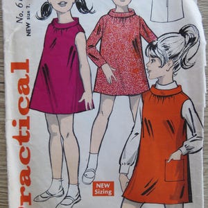 Pode incluir: Um envelope de molde de costura vintage numerado 6111 para tamanhos de 7 a 9 anos. A ilustração apresenta três figuras vestindo vestidos retos sem mangas e de manga comprida com golas altas em cores magenta, vermelho estampado e laranja.