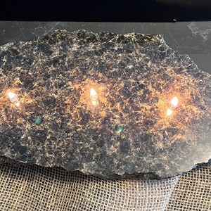 Op de afbeelding: Een zwarte leisteenplaat met drie brandende kaarsen, die een warme en uitnodigende sfeer creëren. De leisteen heeft een natuurlijke, ruwe textuur en is perfect om kaarsen of andere decoratieve items op te presenteren.