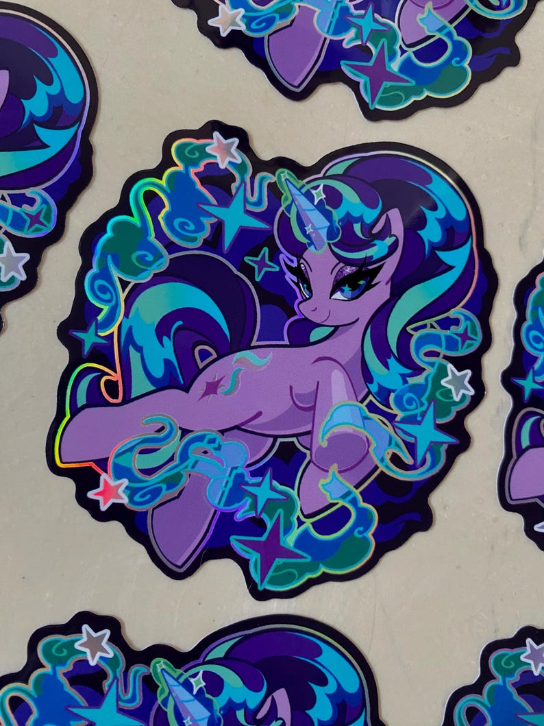 May include: A holographic sticker featuring a purple unicorn with a blue and green mane and tail. The unicorn is surrounded by stars and clouds. The sticker has a glossy finish.