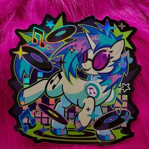 May include: A die-cut sticker featuring a light blue unicorn with a multicolored mane, wearing pink-tinted sunglasses and headphones. The unicorn is surrounded by floating black vinyl records, musical notes, and stars against a dark background.