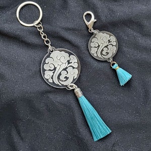 May include: Two silver keychains with a blue tassel. Each keychain features a round, clear acrylic charm with a silver design of a cloud.