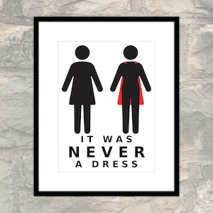 Könnte beinhalten: Gerahmter Druck mit weißem Hintergrund, der zwei schwarze Strichmännchen zeigt. Eine Figur trägt einen roten Umhang. Der Text "IT WAS NEVER A DRESS" steht unter den Figuren. Der Rahmen ist schwarz.