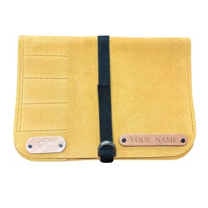 May include: A tan leather tool roll with multiple slots for tools. The roll has a black strap with a metal buckle and a personalized nameplate that says "YOUR NAME".