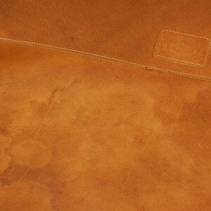 May include: Close-up of a brown leather surface with a stitched seam and a small rectangular patch of leather. The leather has a worn, distressed look.
