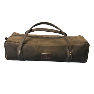 May include: A brown duffel bag with two handles and a zipper closure. The bag has a rectangular shape and a leather patch with a logo. The handles are attached with metal rivets. The bag is made of a durable material.
