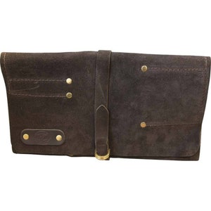 May include: A brown leather tool roll with multiple pockets and a buckle closure. The roll has brass rivets and stitching.