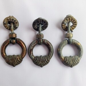 May include: Three antique brass drawer pulls with a ring design. The pulls have a worn, aged finish and are in good condition.