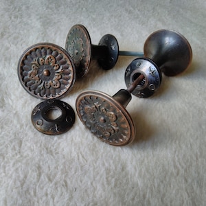 May include: Four antique bronze door knobs with ornate floral designs. The knobs have a round base and a small, round knob on top. The knobs are in good condition and have a patina finish.